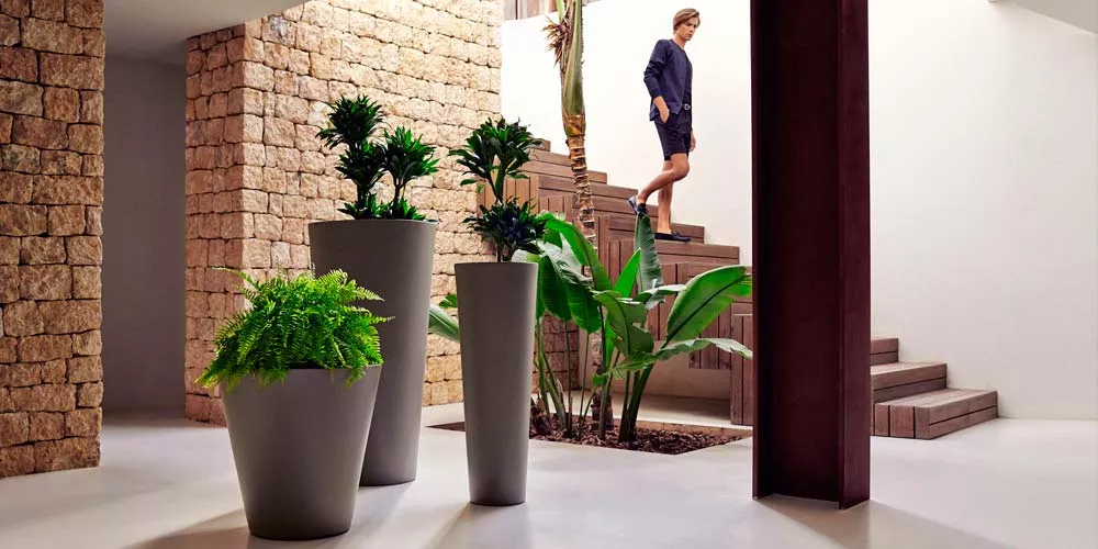Vondom Studio Planters Pflanzkübel in Grau, verschiedene Größen, in modernem Innenraum mit Steinwand und Treppe im Hintergrund.