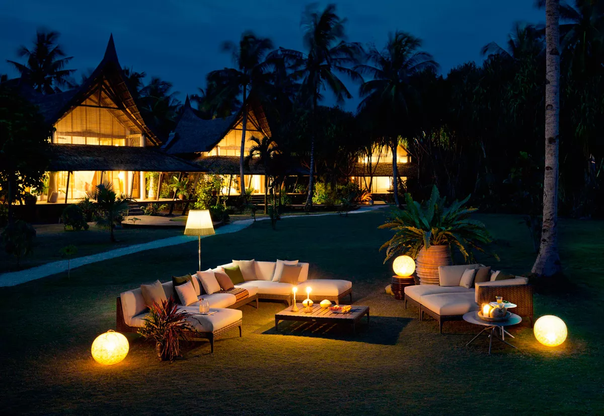Dedon Mu Kollektion zeigt eine gemütliche Outdoor-Lounge bei Nacht mit beleuchteten Möbeln und tropischem Hintergrund ideal für entspannte Abende