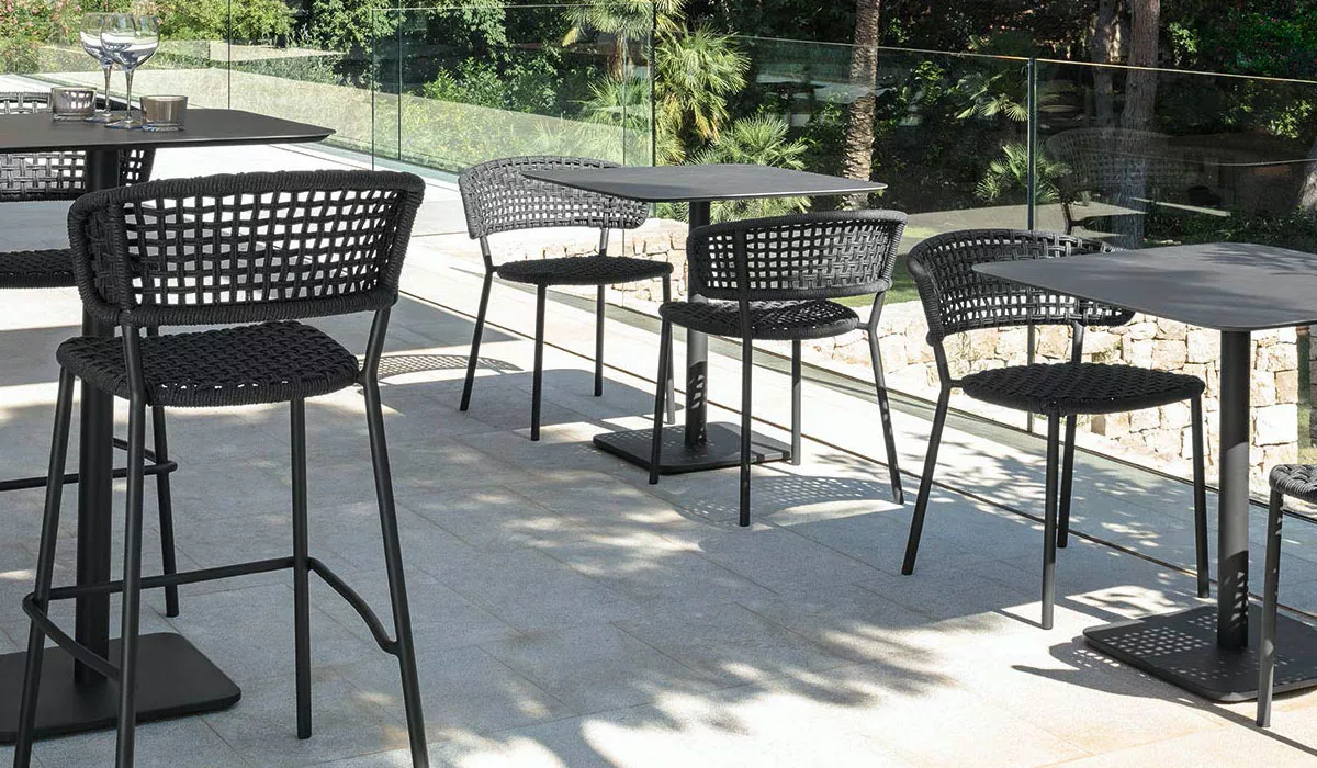 Talenti Essplatzmöbel in Schwarz auf einer sonnigen Terrasse mit Glasgeländer und grüner Gartenkulisse.