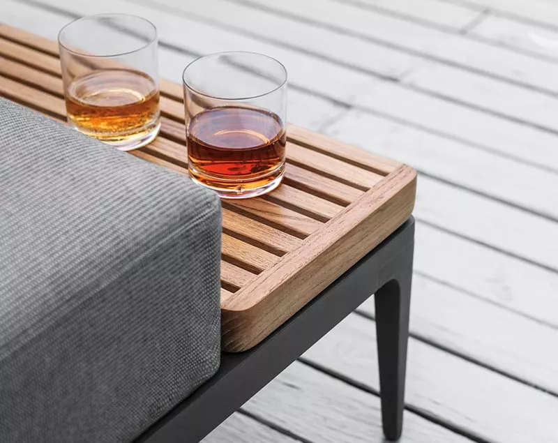 Zwei Gläser mit Getränken auf einer Holzbank mit grauem Polster auf einer Terrasse aus hellem Holz.