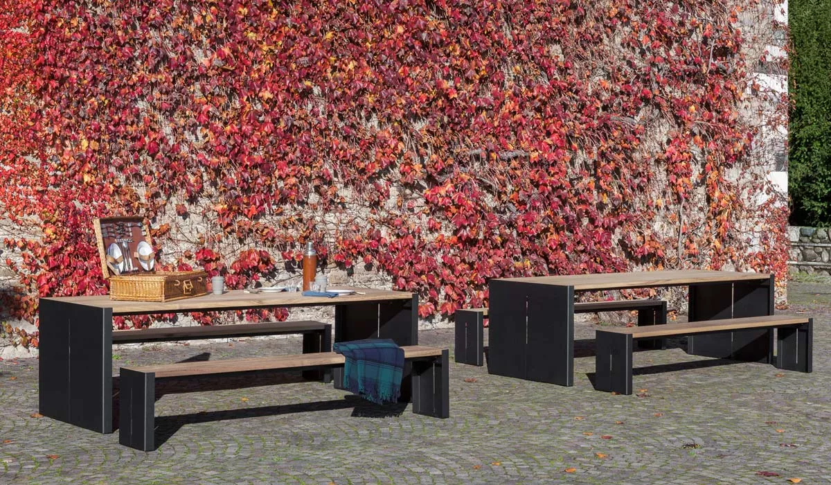 Essgruppe von Lapalma PANCO in Schwarz und Holzoptik, bestehend aus zwei Bänken und einem Tisch, im herbstlichen Gartenhintergrund.