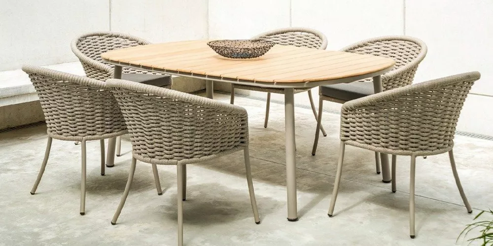 Sechsteiliges Alexander Rose Cordial Gartenmöbel-Set in Beige mit ovalem Holztisch und geflochtenen Stühlen auf Betonboden.