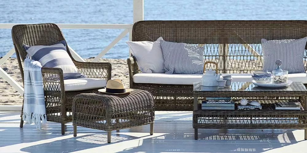 Sika-Design Dawn Loungegruppe in Braun auf einer Terrasse am Meer, bestehend aus Sofa, Sessel und Tisch, mit Kissen und Decke dekoriert.