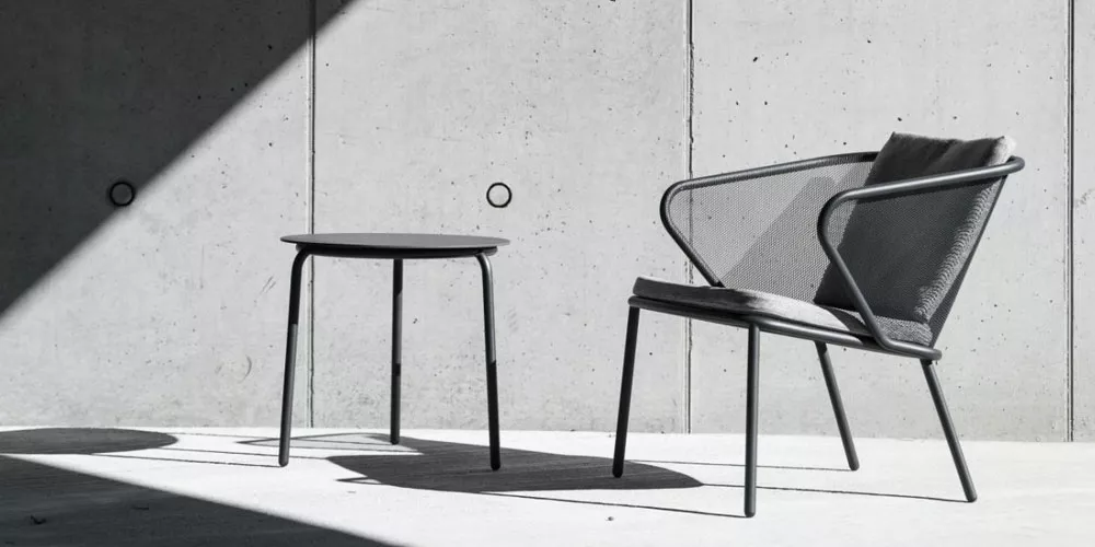 Grau-schwarzer Todus Condor Stuhl und Tisch auf Betonboden in minimalistischem, modernem Ambiente.