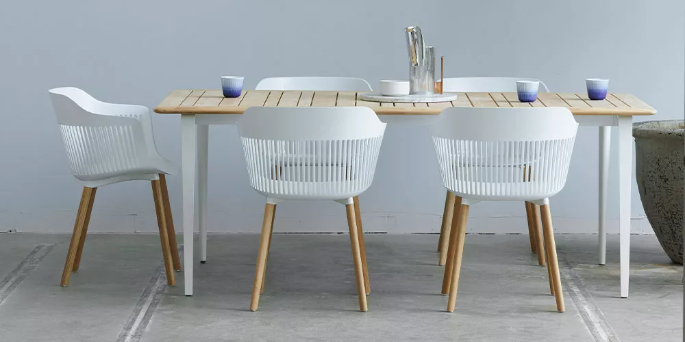 Dedon Kollektion Aiir zeigt einen Esstisch mit vier weißen Stühlen und einer Tischdekoration in einem modernen Raum ohne Hintergrund