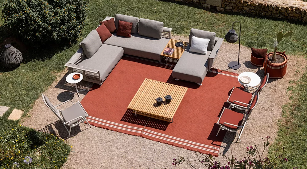 Luftaufnahme einer grauen Dedon Mbrace Outdoor-Sofagarnitur mit rotem Teppich auf einer Terrasse im Garten.