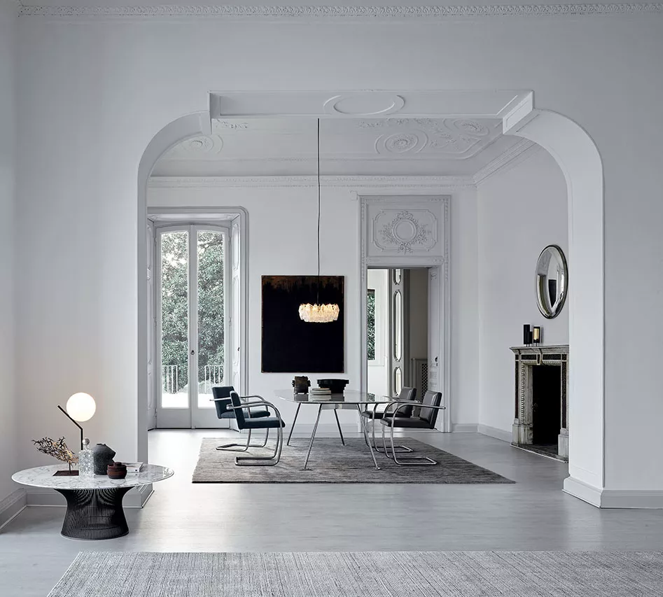 Ein elegantes Wohnzimmer mit dem Knoll Grasshopper Tisch und modernen Stühlen in einem hellen Raum mit hohen Decken und einem Kamin im Hintergrund.