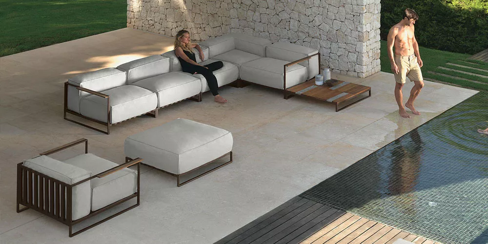 Talenti Casilda Kollektion in Beige auf einer Terrasse am Pool, bestehend aus Sofas und Hocker mit Holz- und Metallrahmen, entspannte Stimmung.