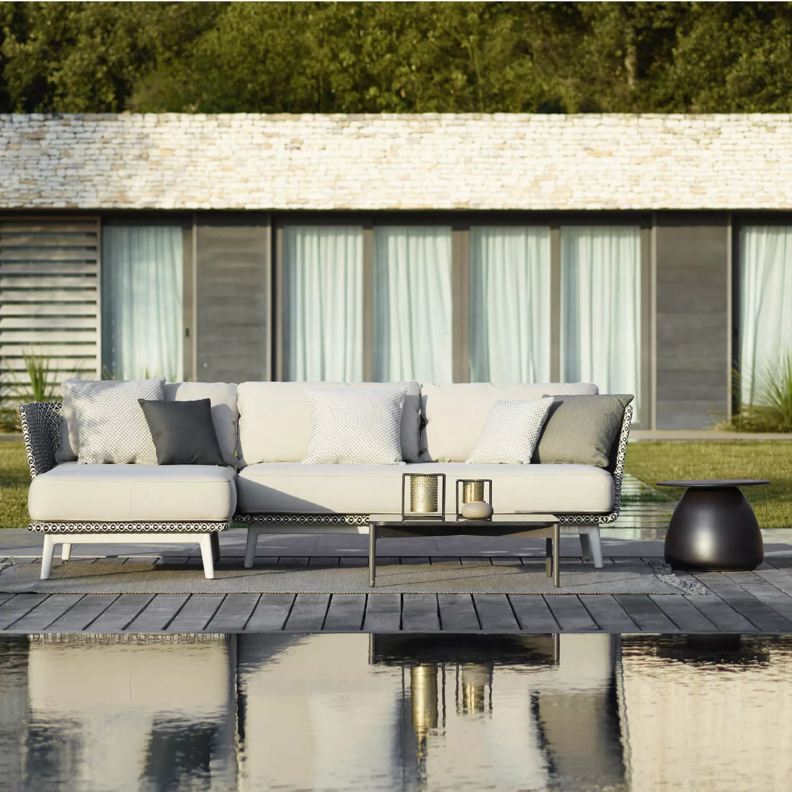 Dedon Mbarq Lounge Sofa in einem modernen Garten am Pool mit Kissen und Dekorationen vor einem Haus mit großen Fenstern und Vorhängen