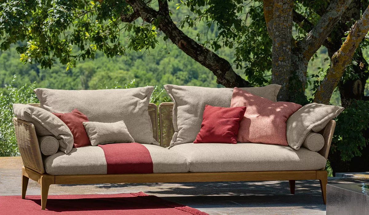 Talenti Loungemöbel in Beige und Rot auf einer Terrasse mit grünem Hintergrund, umgeben von Bäumen, als stimmungsvolles Outdoor-Bild.