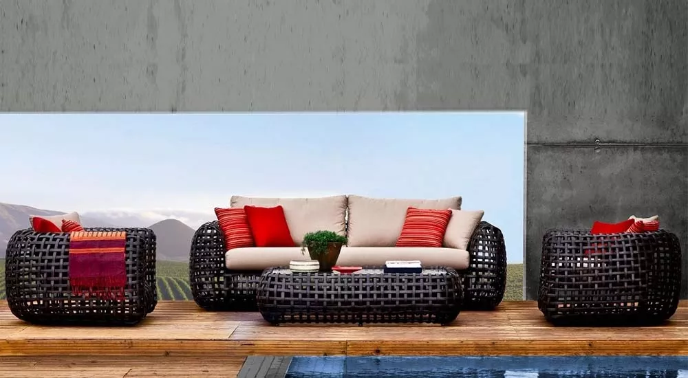 Kenneth Cobonpue Matilda Loungegruppe in Schwarz mit beigen Kissen und roten Akzenten, auf Holzterrasse vor Betonwand und Bergkulisse.