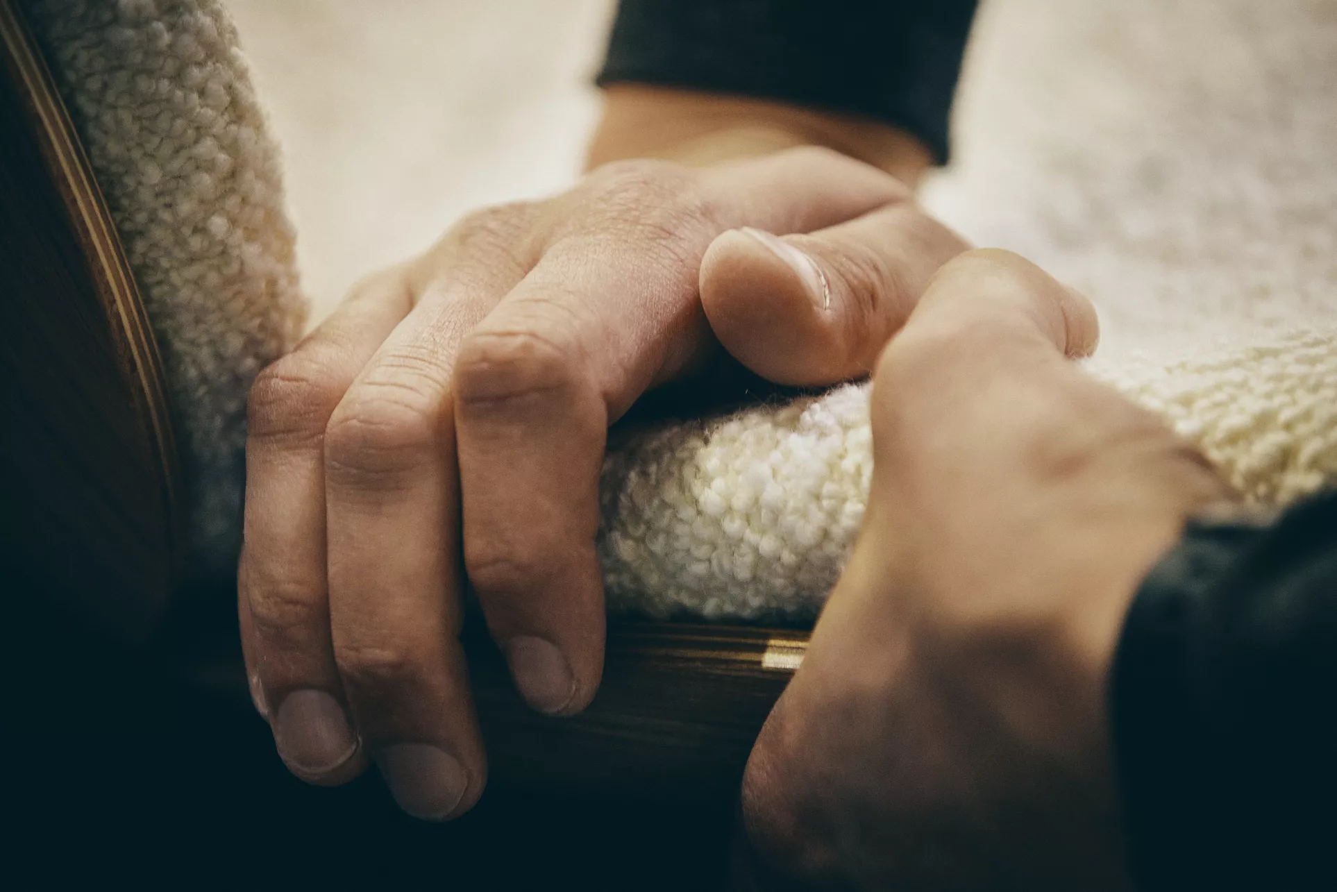 Hände berühren weichen, cremefarbenen Stoff in Nahaufnahme, stimmungsvolles Bild mit Fokus auf Textur und Material.