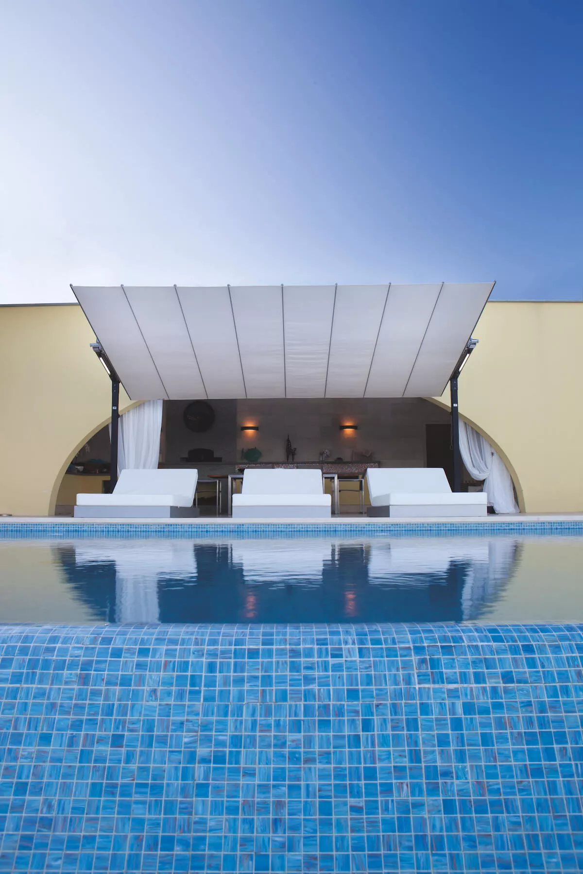 FIM Flexy Sonnendach-Markise in Weiß, 250 x 428 cm, über einem modernen Pool mit blauem Mosaik, vor einem eleganten Gebäude.