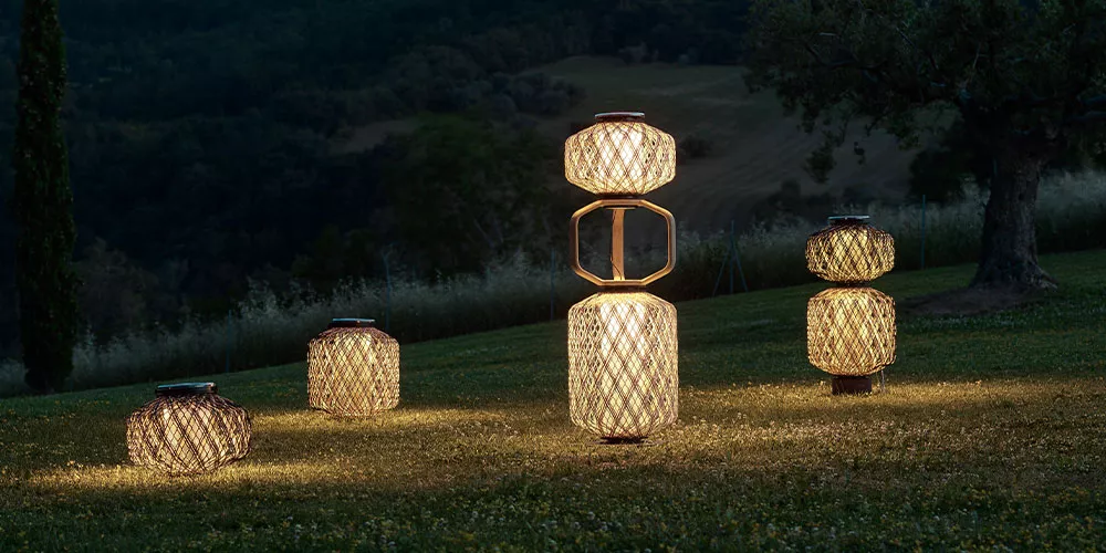 Dedon Leuchten aus der Kollektion leuchten im Freien auf einer Wiese bei Dämmerung im Hintergrund sind Bäume und Hügel zu sehen