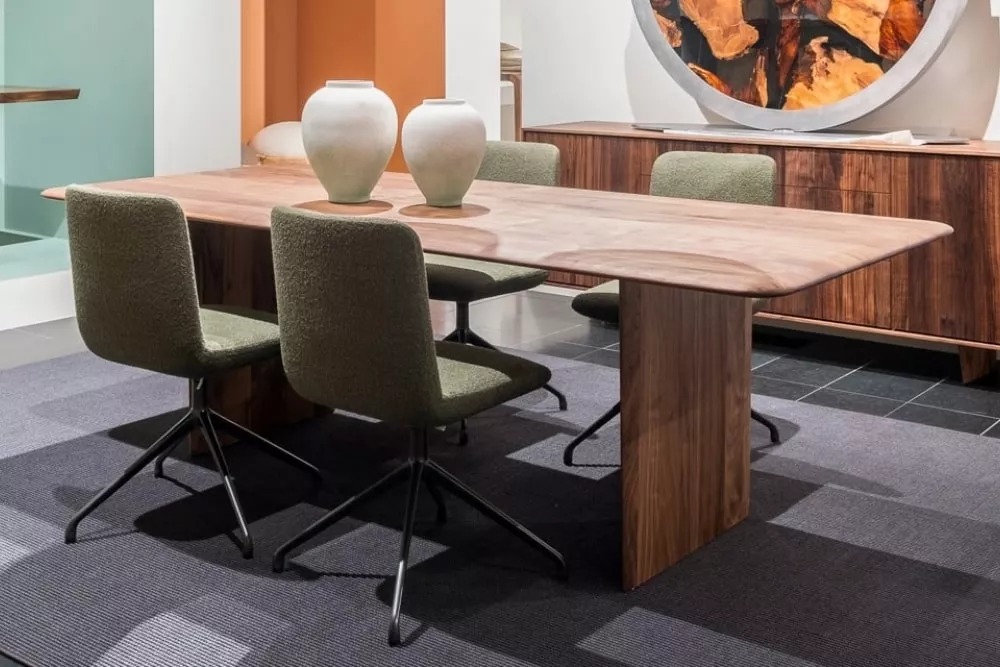 RIVA1920 Tisch in Holzoptik mit zwei weißen Vasen, umgeben von vier olivgrünen Stühlen, auf einem grauen Teppich in modernem Raum.