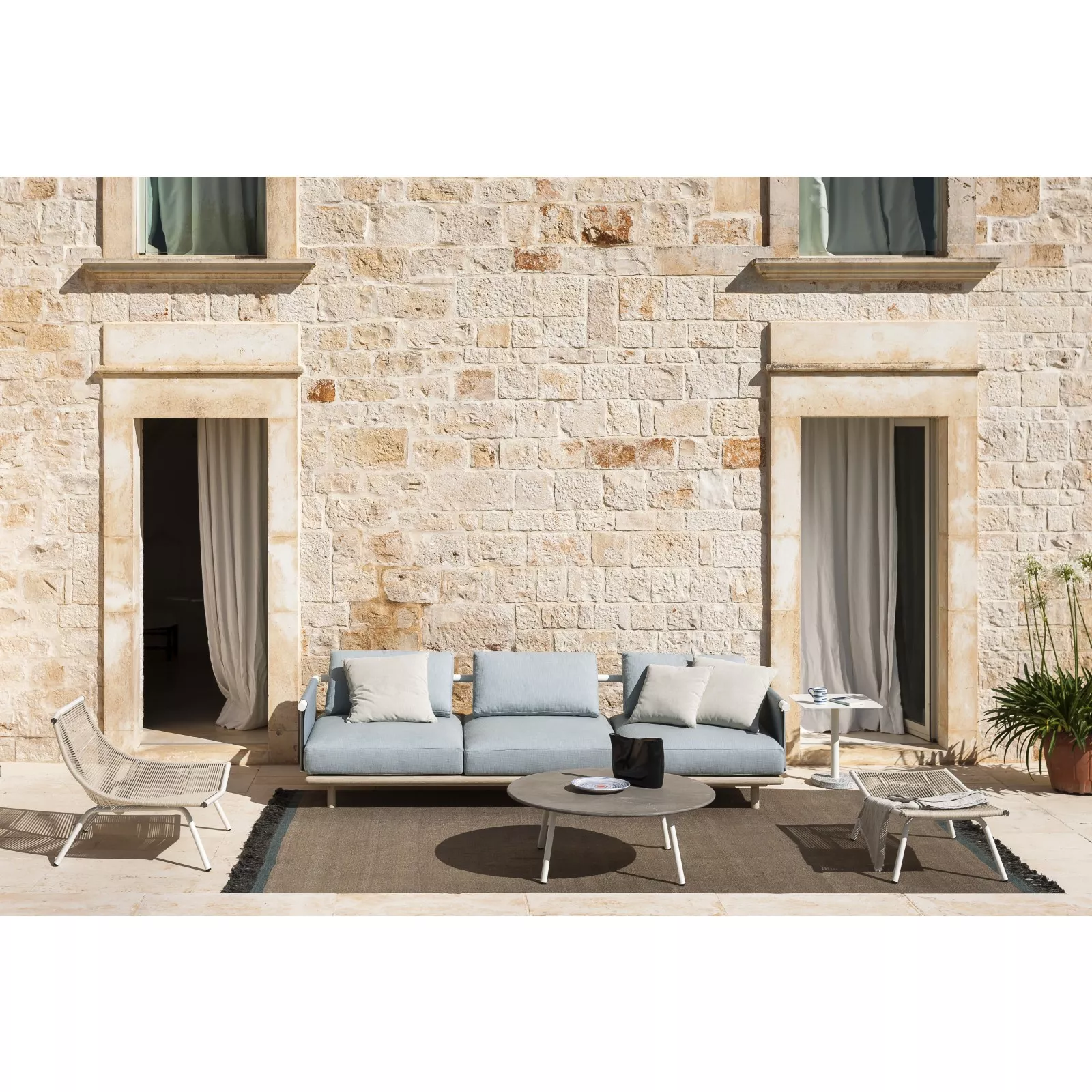 Roda Eden Kollektion, hellblaue Outdoor-Sofas und Sessel auf einer Terrasse vor einer Steinwand, stimmungsvolles Ambiente.