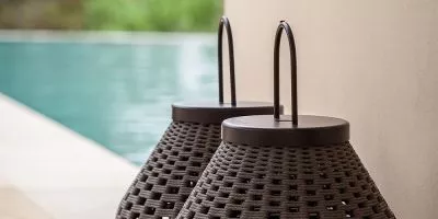 Zwei Poltrona Frau Gartenleuchten in Dunkelbraun stehen nebeneinander auf einer Terrasse mit Blick auf einen Pool.