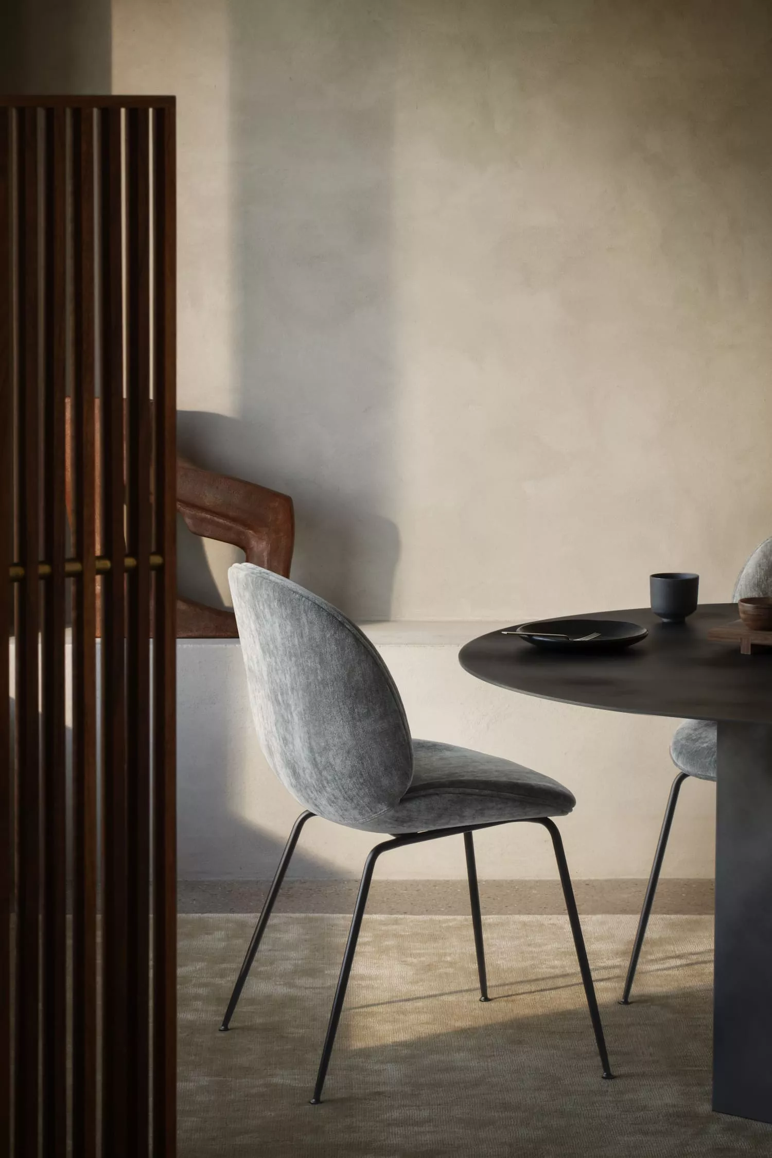 Beetle Stuhl von GamFratesi in grauem Stoff, vor einem runden Tisch in einem modernen, minimalistisch eingerichteten Raum.