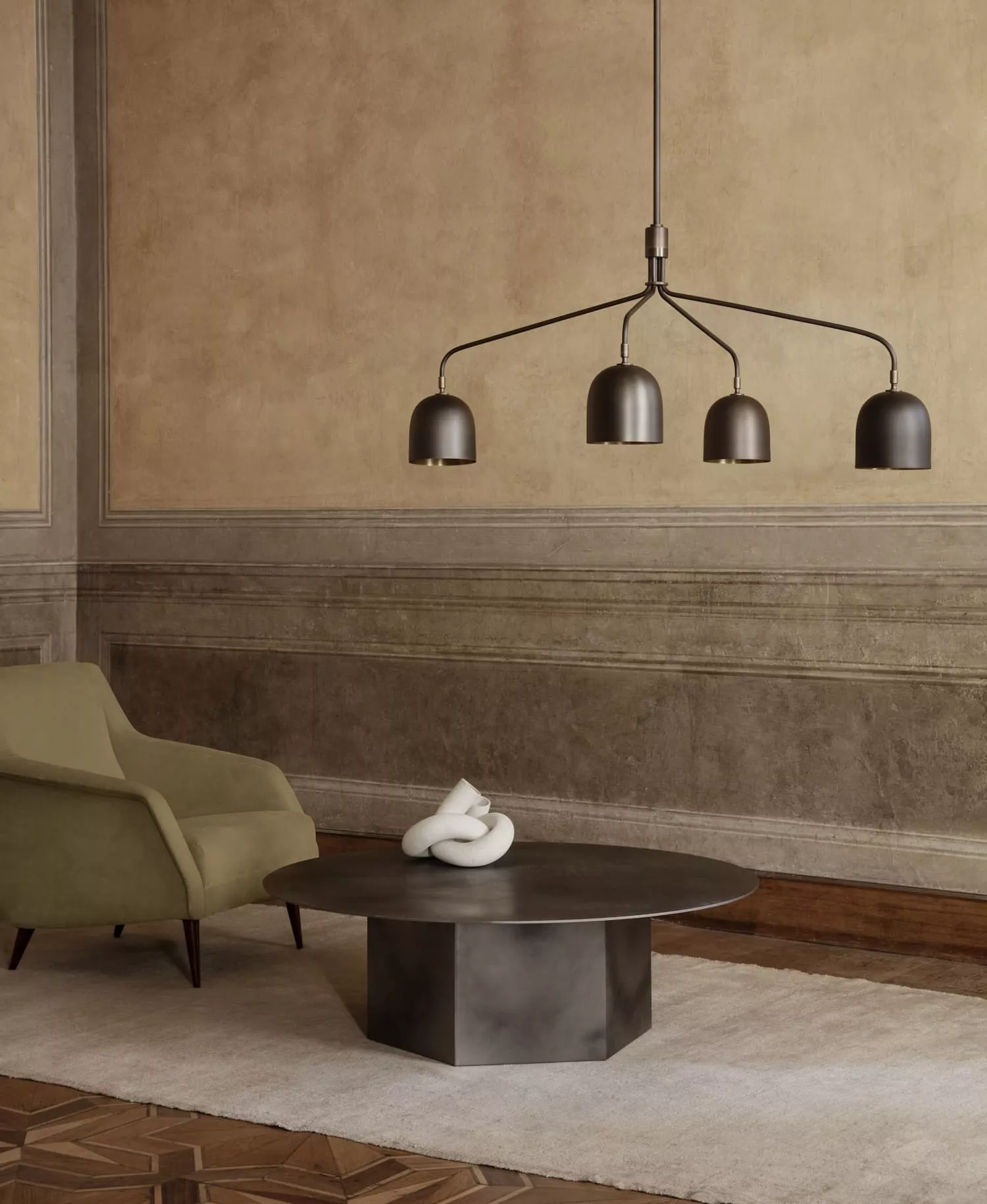 Ein Wohnzimmer mit einem grünen Sessel einem runden Couchtisch und einer Gubi Pendelleuchte in einem eleganten Ambiente.