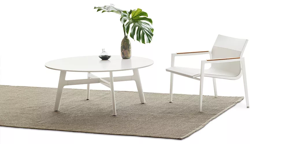 Dedon Kollektion Vid zeigt einen weißen Tisch und Stuhl auf einem Teppich mit einer Vase und Pflanze als Dekoration ohne Hintergrund