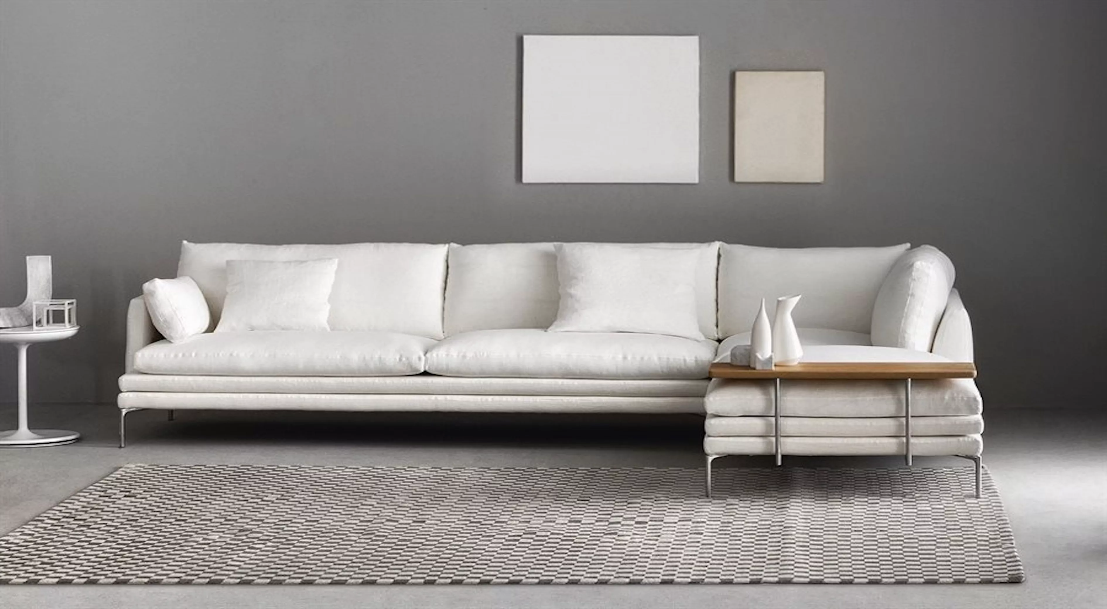 Ein weißes William-Sofa von Villa Schmidt in einem modernen Wohnzimmer mit grauem Hintergrund und geometrischem Teppich.
