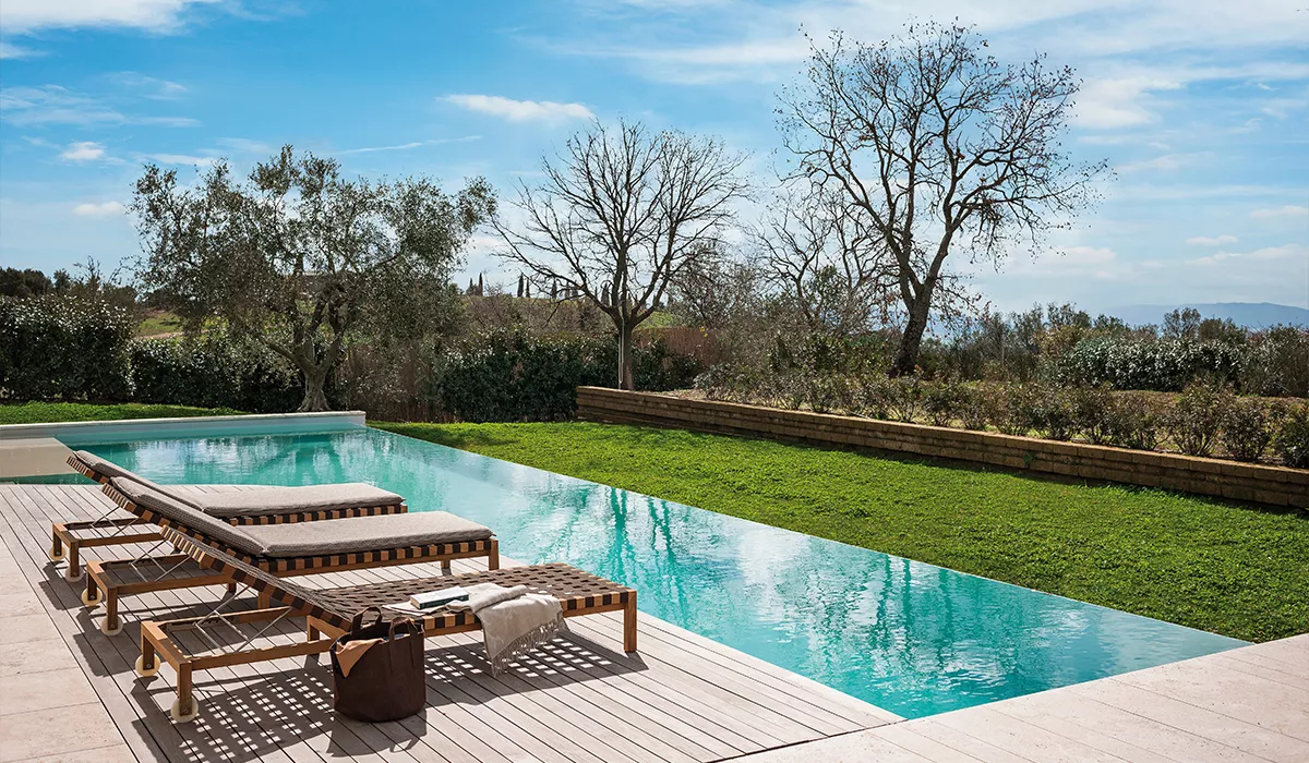 Zwei Roda Sonnenliegen in Naturholz auf einer Terrasse am Pool mit Blick auf einen Garten und blauen Himmel.