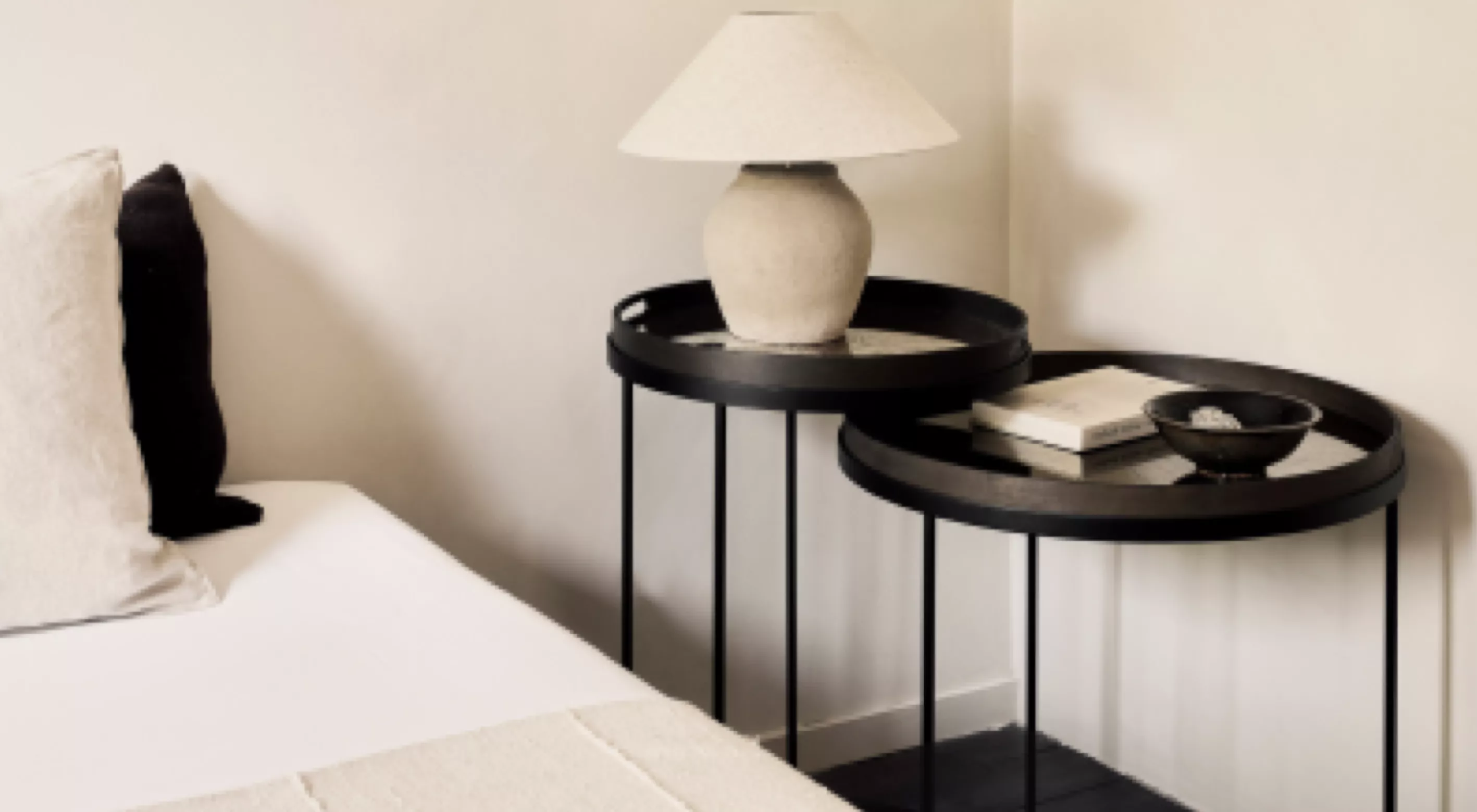 Zwei schwarze Beistelltische von Villa Schmidt mit runden Tabletts, darauf eine beige Lampe und Bücher, vor einer weißen Wand.