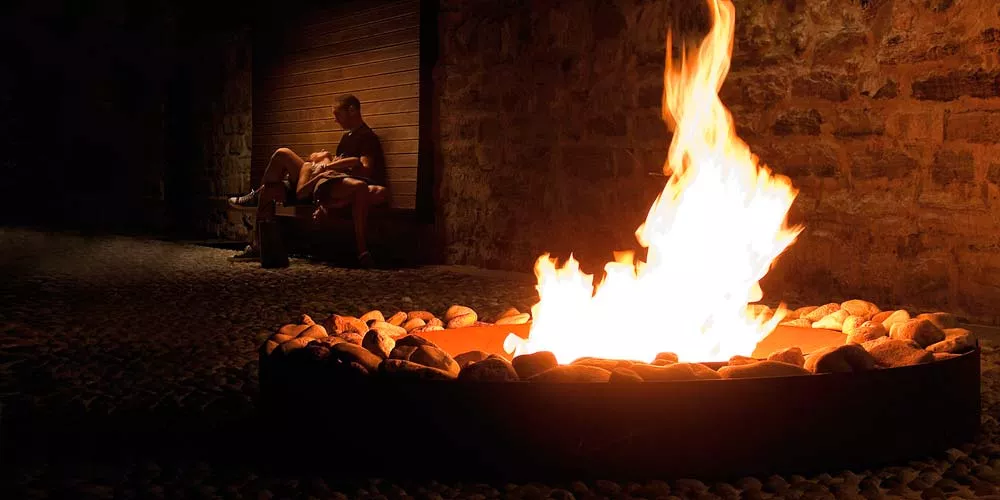 Ein Mann sitzt auf einer Bank und liest ein Buch während ein großes Feuer in der Ak-47 Feuerstellen Zen brennt stimmungsvolles Bild bei Nacht
