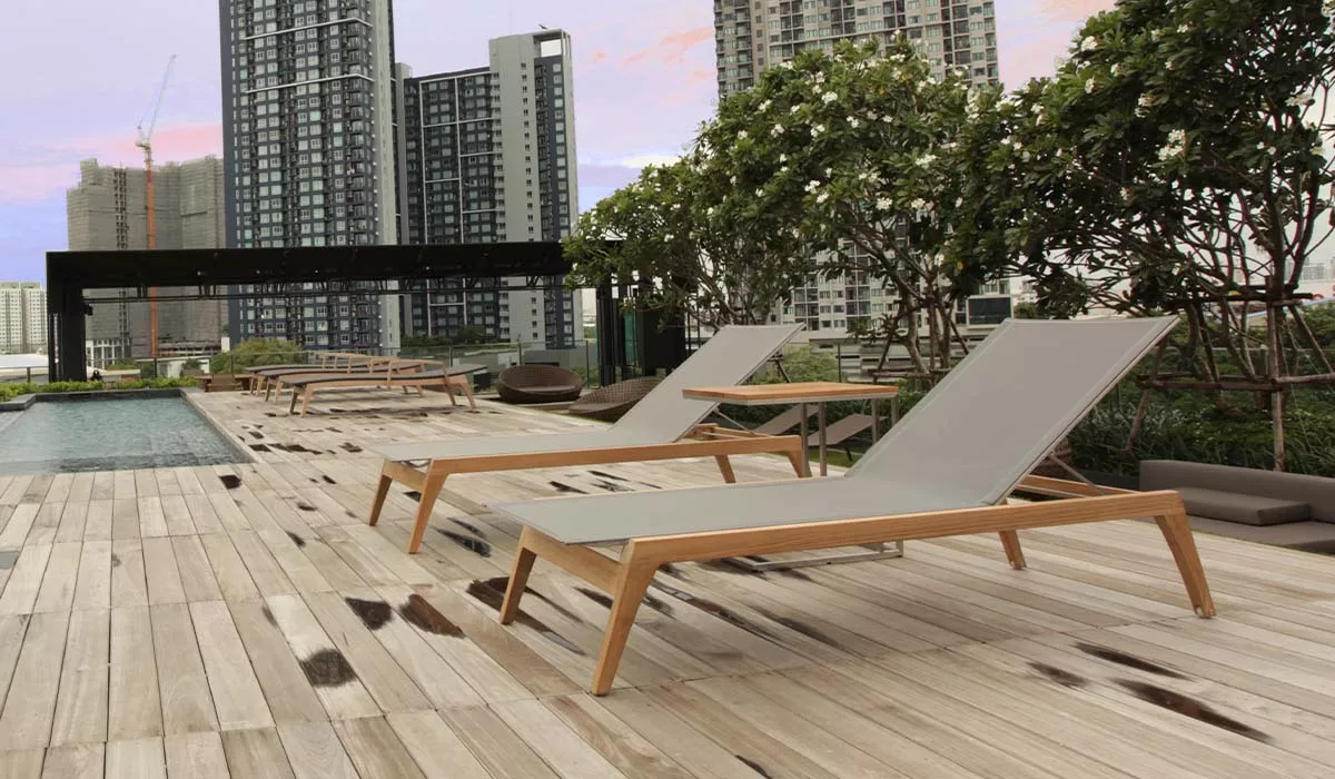 Zwei Royal Mirage Liegen in Grau auf einer modernen Dachterrasse mit Holzboden und Stadtblick bei Sonnenuntergang.