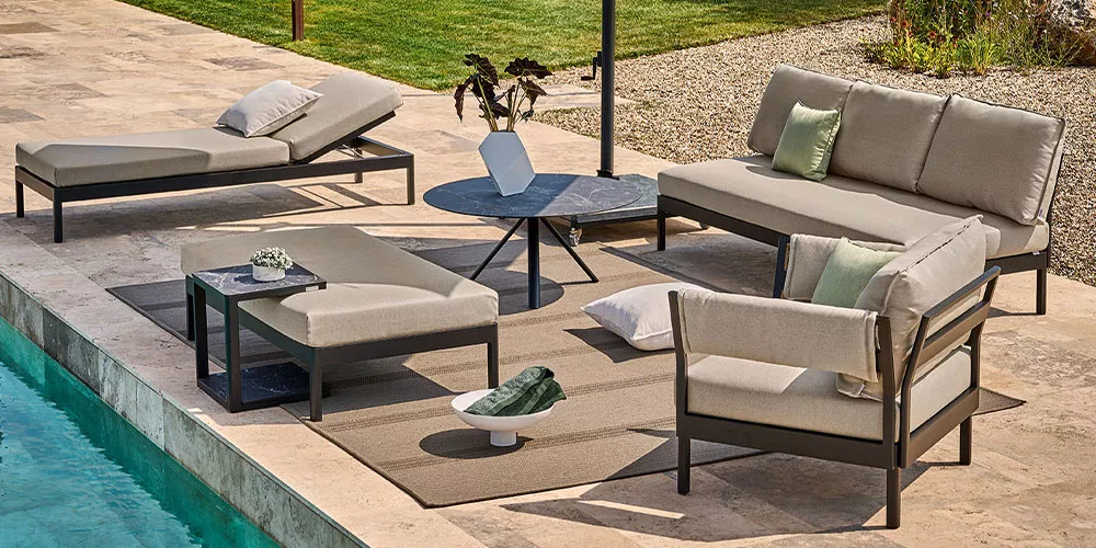 Weishäupl Minu Gartenmöbel-Set in Beige auf einer Terrasse am Pool, bestehend aus Sofa, Liege und Tisch, umgeben von grüner Rasenfläche.
