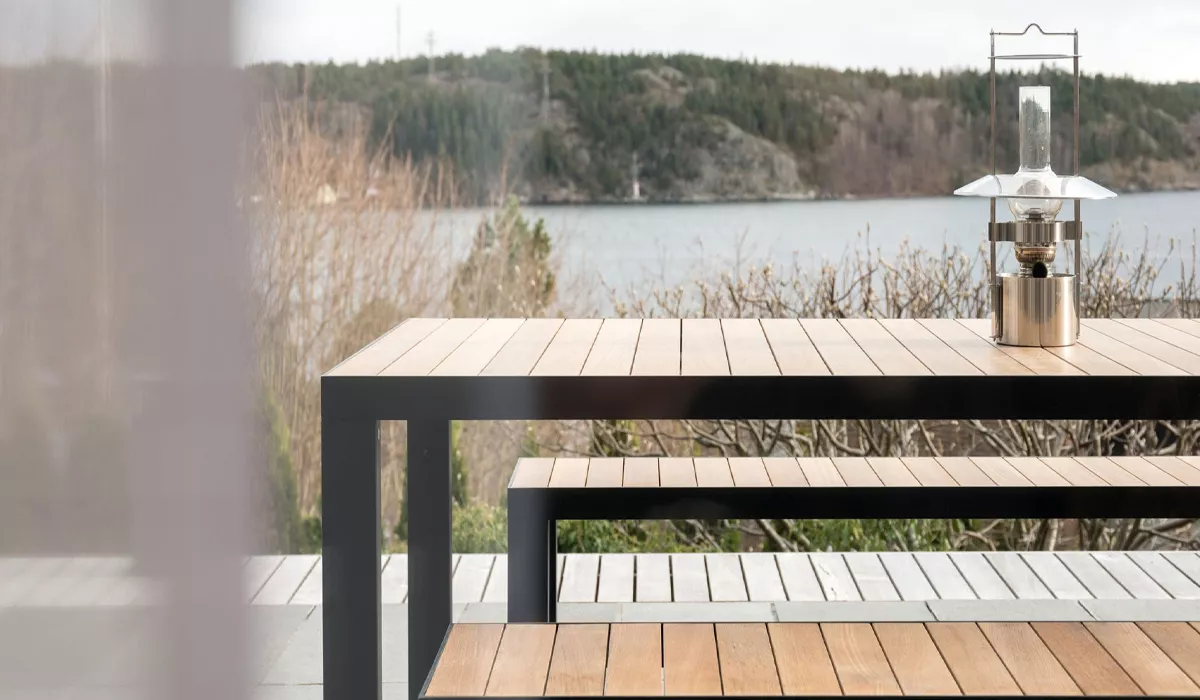 Roshults Tisch und Bank aus Holz und Metall in natürlicher Umgebung mit Seeblick, stimmungsvolles Bild.