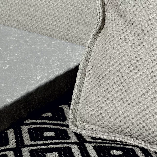 Nahaufnahme des B&B Italia I Oh It Rains Sessels in grauem Stoff auf einem gemusterten Teppich und neben einer Steinplatte