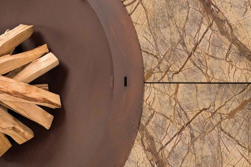 AK47 Ercole Feuerstelle aus Marmor Rain Forest Brown und Stahl in Small 150 cm mit Holzstapeln auf einer Marmorplatte