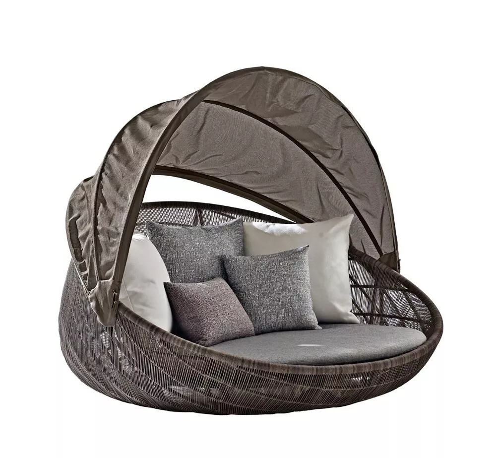 B&B Italia Canasta 13 Outdoor Sofainsel mit Rollen 180 cm in einem mood Bild mit mehreren Kissen und einem Sonnenschutz in einem Garten.