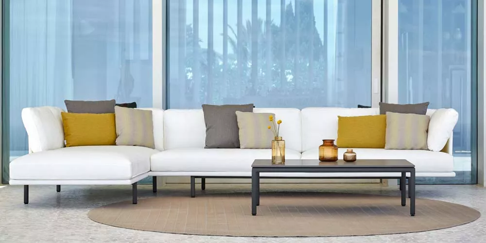 Point Long Island Outdoor Loungegruppe in Weiß mit gelben und grauen Kissen, auf einer Terrasse vor einer Glasfassade.