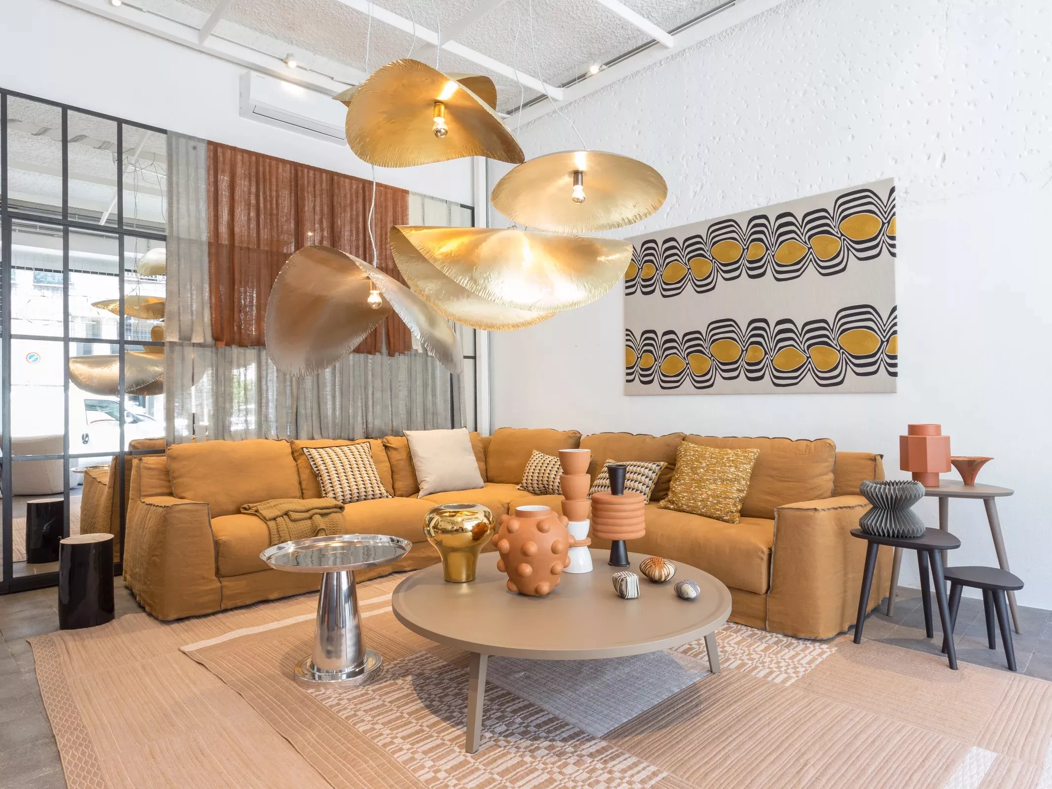 Ein Wohnzimmer mit einer großen beigen Gervasoni Couch und modernen Dekorationen wie goldenen Lampen und bunten Kissen in einem stilvollen Ambiente.