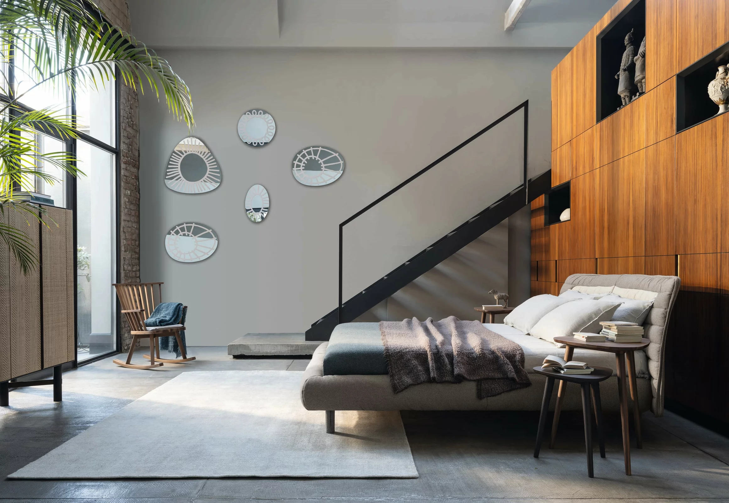 Ein modernes Schlafzimmer mit einem Gervasoni Bett und stilvollen Möbeln in einem hellen Raum mit Treppe und dekorativen Spiegeln an der Wand.