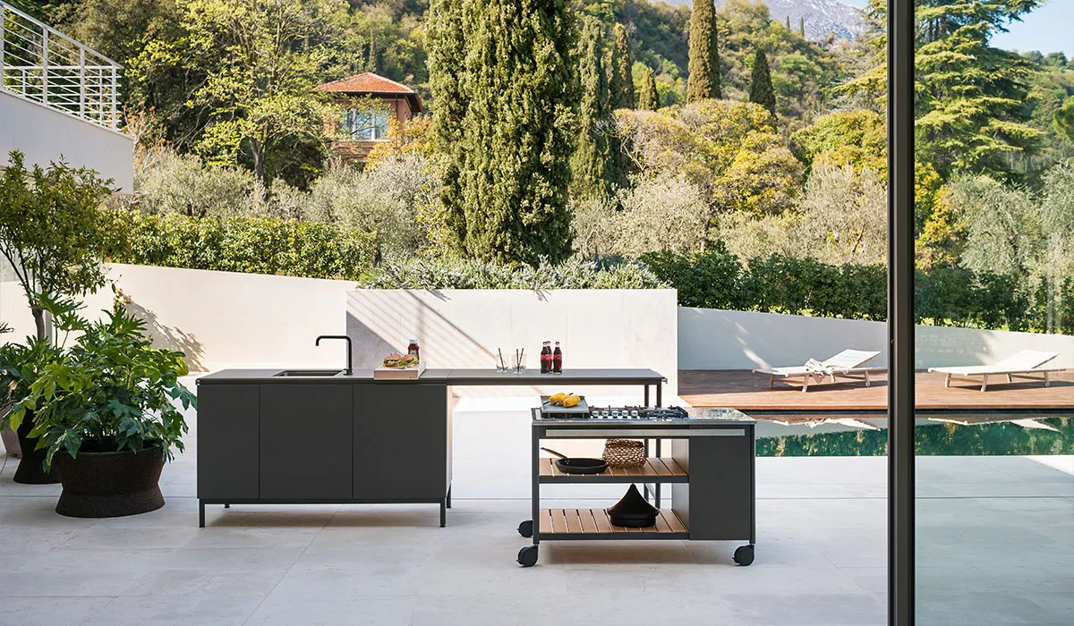 Roda Outdoor-Küche in Anthrazit vor einem Pool mit mediterranem Garten im Hintergrund, technische Details nicht sichtbar.