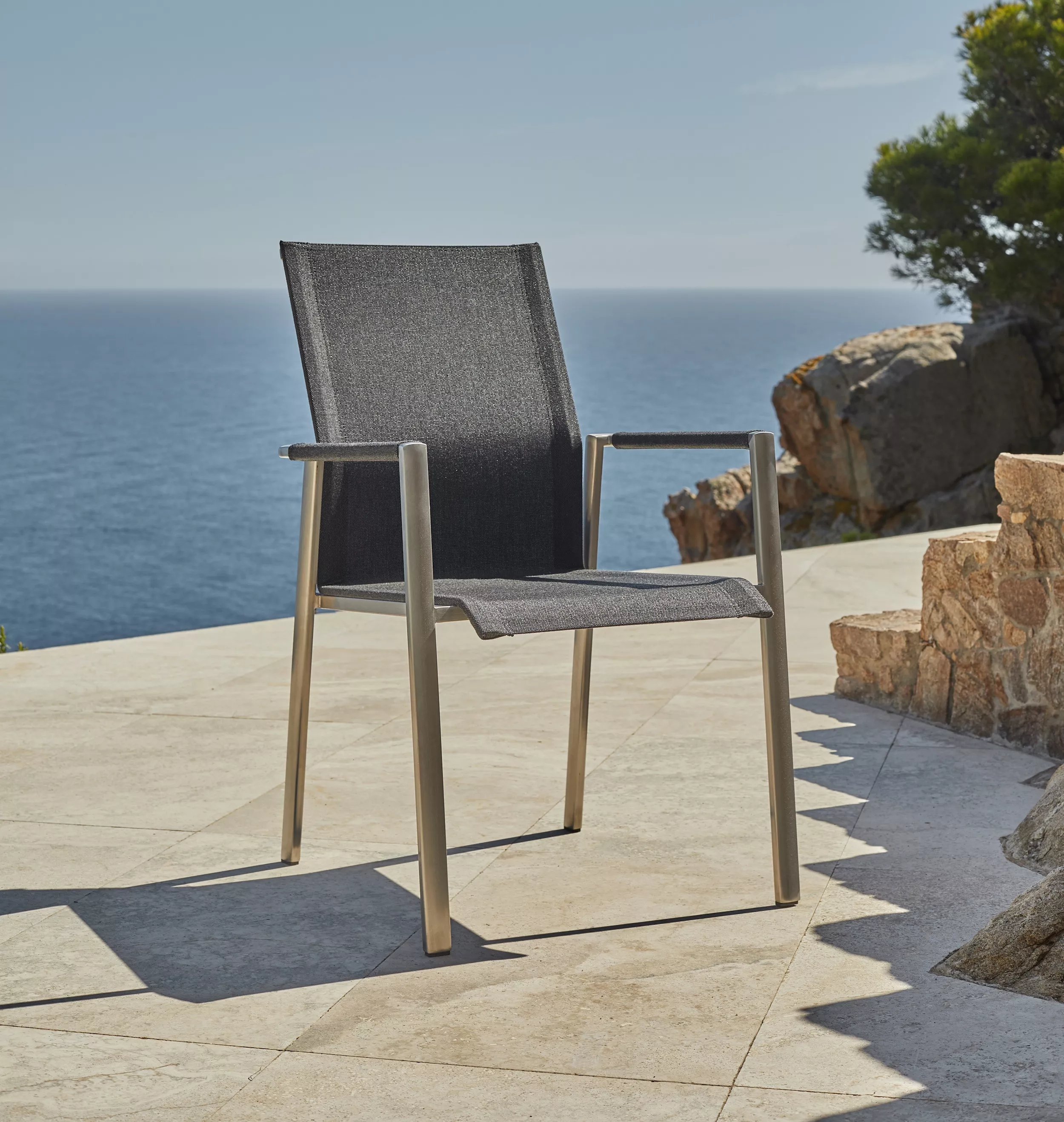 Solpuri Dance Stuhl auf einer Terrasse mit Meerblick und Felsen im Hintergrund Mood Bild