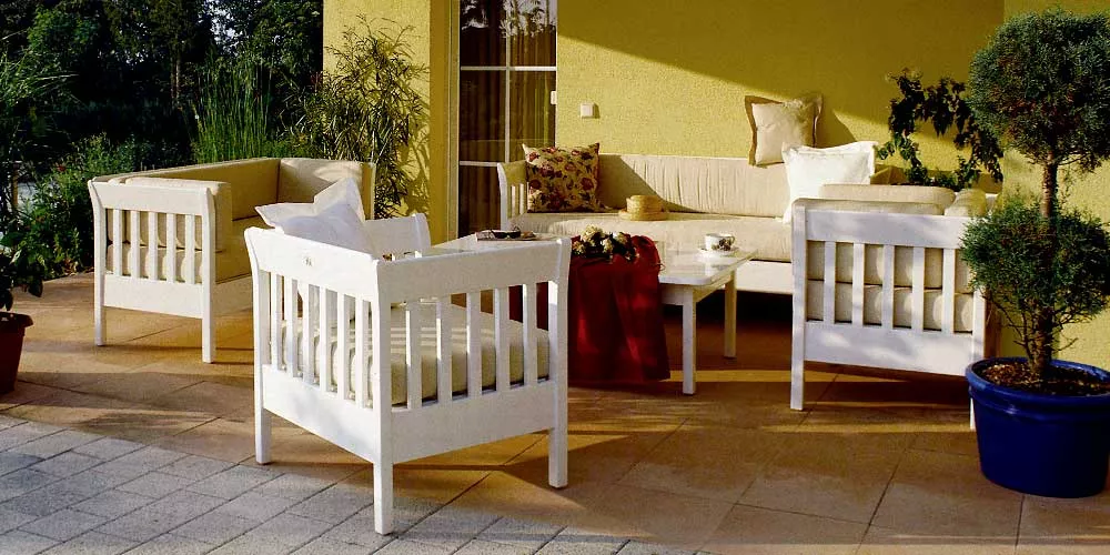 Herrenhaus Frederic Loungegruppe in Weiß auf einer sonnigen Terrasse mit gelbem Hintergrund und Pflanzen im Vordergrund.