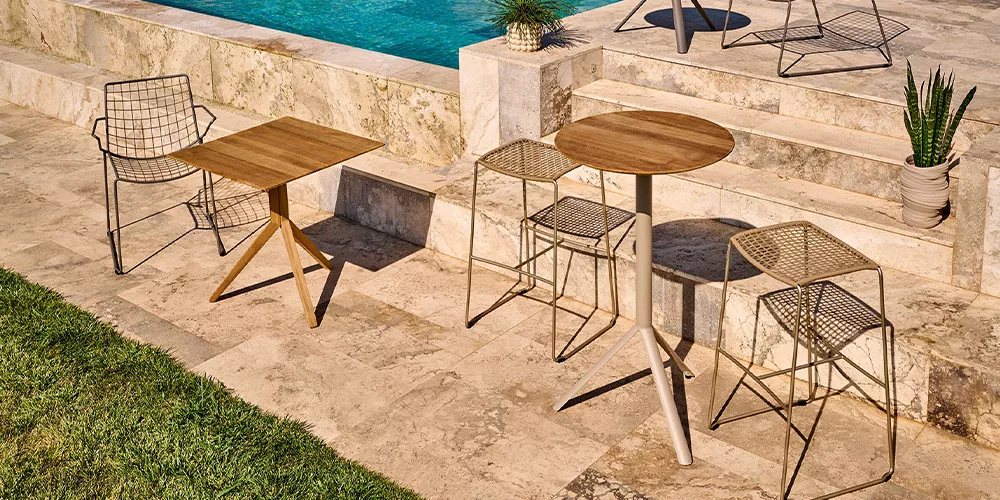 Weishäupl Trio Gartenmöbel-Set in Naturtönen auf einer Terrasse am Pool, bestehend aus zwei Tischen und vier Stühlen, in sommerlicher Atmosphäre.