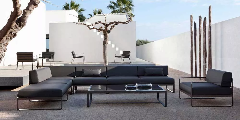 Bivaq Sit Loungegruppe in Anthrazit auf einer modernen Terrasse mit weißem Hintergrund und Palmen im Hintergrund.