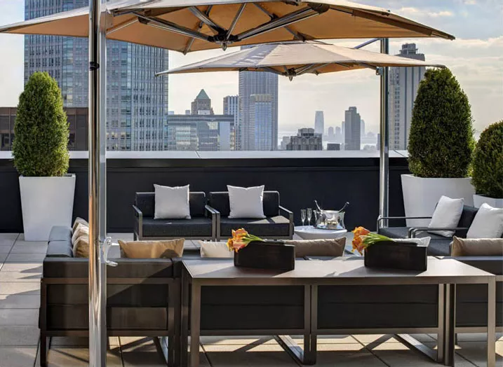 Tuuci Sonnenschirm Bay Master Cantilever in Beige auf einer modernen Dachterrasse mit Stadtblick und eleganten Sitzmöbeln.
