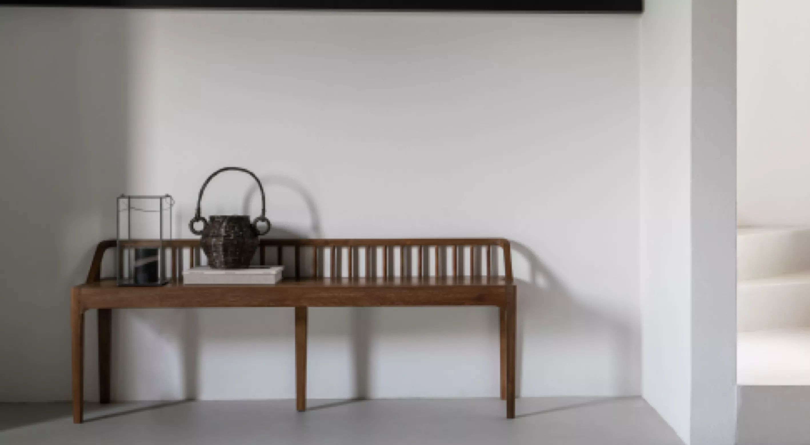 Holzbank von Villa Schmidt in natürlichem Braun vor weißer Wand, dekoriert mit einem Korb und Büchern, minimalistische Raumgestaltung.