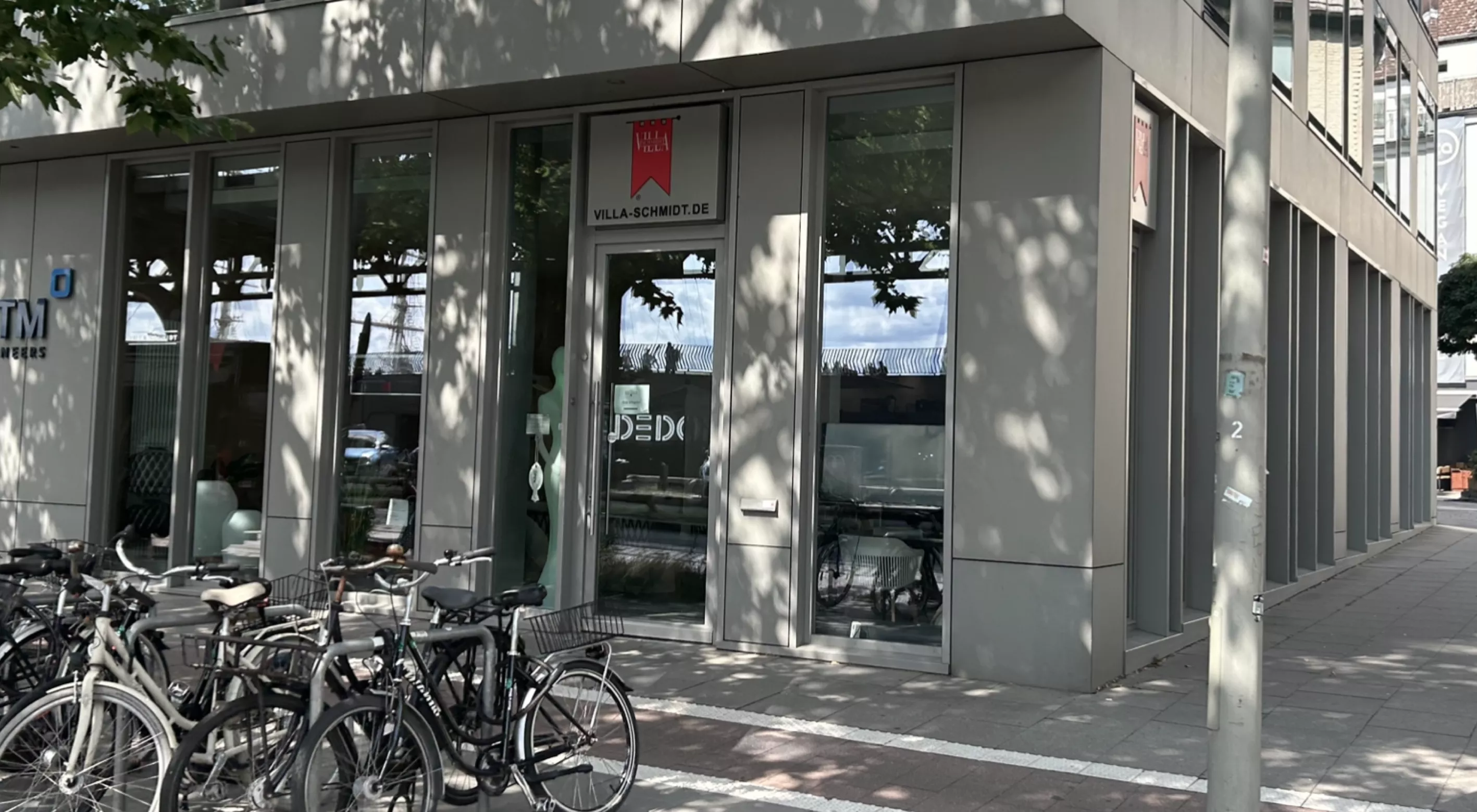 Fahrräder stehen vor dem modernen Gebäude von Villa Schmidt mit großen Fenstern und einem roten Schild, das den Eingang markiert.