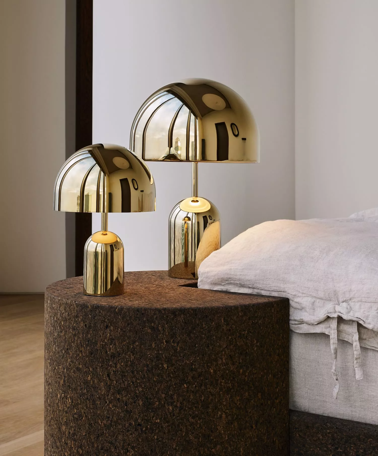 Tom Dixon Portable LED-Lampe in Gold auf einem runden Tisch neben einem Bett in einem modernen, minimalistischen Raum.