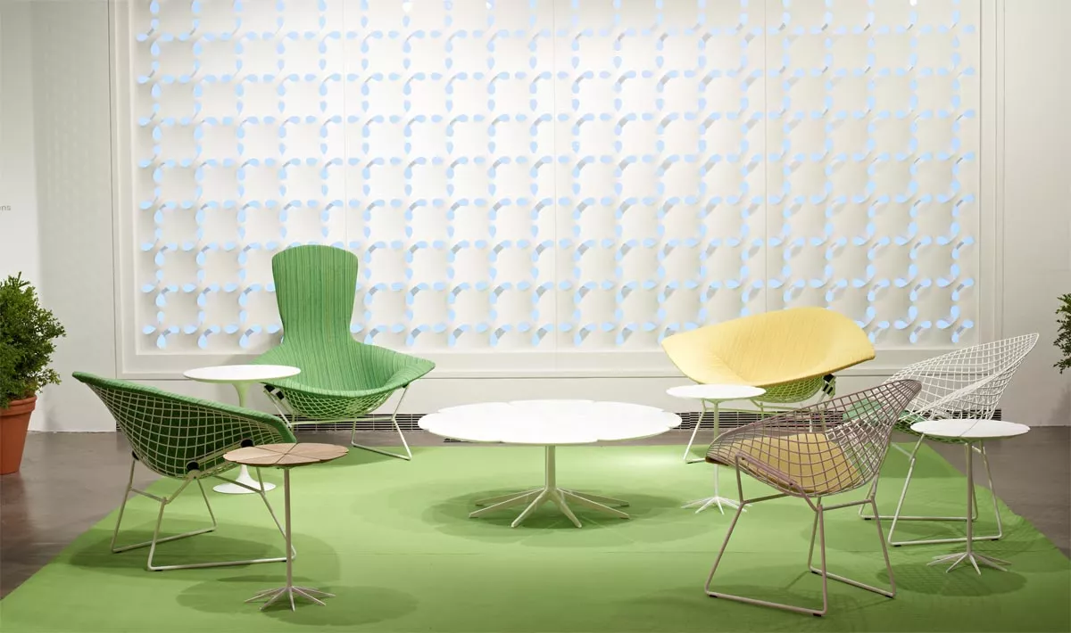 Knoll Studio Petal Beistelltisch in einem modernen Raum mit grünen und gelben Stühlen auf einem grünen Teppich vor einer dekorativen Wand.