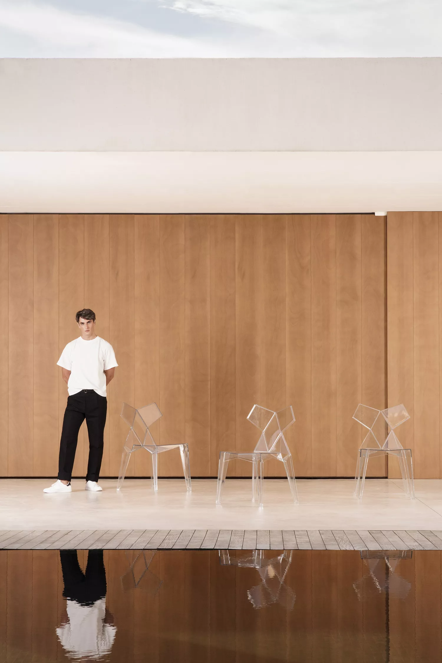 Ein Mann geht an einem Pool entlang, vorbei an Vondom Kimono Stühlen von Ramon Esteve, auf einer Terrasse mit Holzwand im Hintergrund.