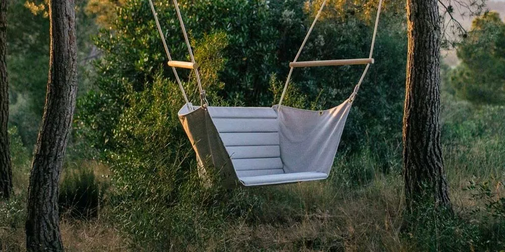 Hängesessel Calma Marea in Grau zwischen Bäumen, stimmungsvolles Bild im Wald bei Sonnenuntergang.