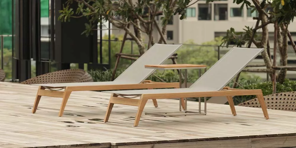 Zwei Royal Mirage Monaco Liegestühle in Holzoptik mit grauem Stoff auf einer Terrasse mit urbanem Hintergrund.
